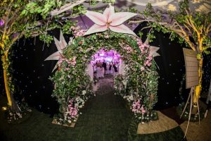 Tunnel made of flowers and foliage with large pink flowers artificial trees surrounding